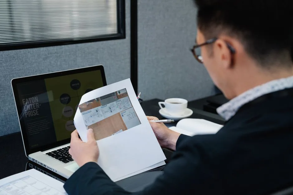 Homme se concentrant intensément tout en examinant des documents à un bureau avec un ordinateur portable.